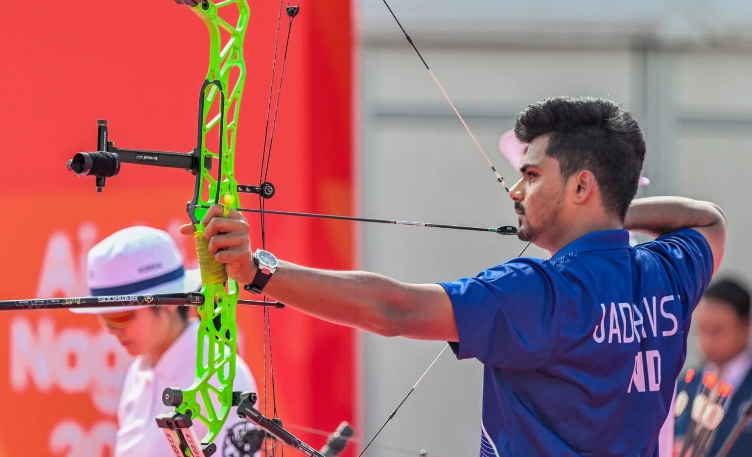 An archer in a blue shirt aims a neon green compound bow to the right.