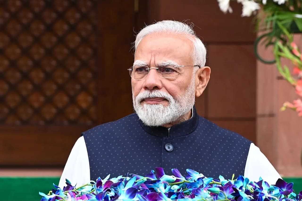 A man with white hair and beard wears glasses and a dark blue vest.