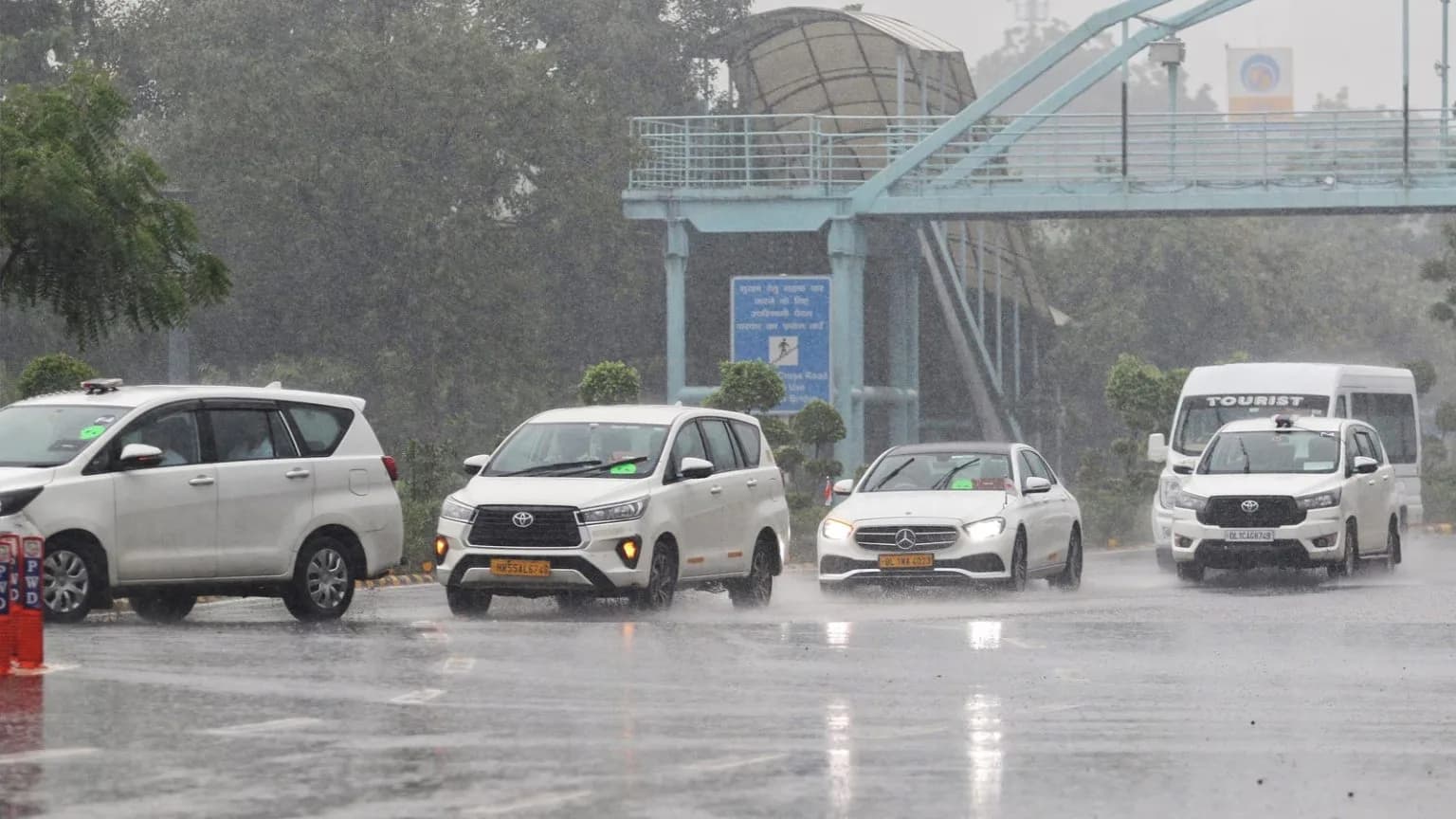 Cars driving on a wet road during a heavy rain shower, with an overpass in the background.