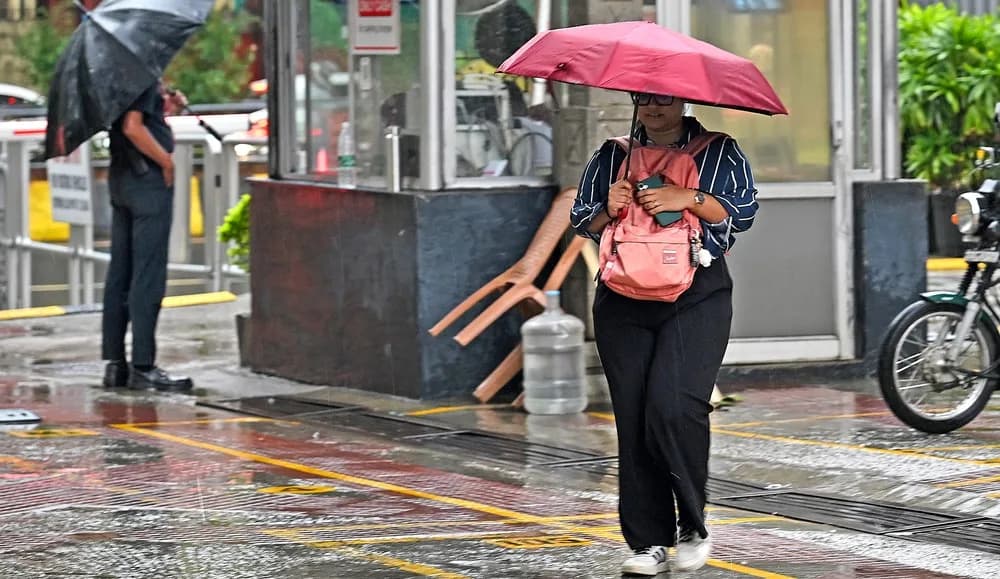 A woman with a pink umbrella and backpack walks on a wet street during rain.