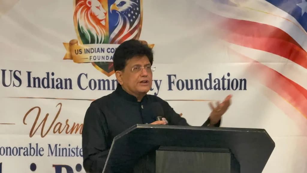 A man in a black shirt and glasses speaks at a podium with a banner behind him.