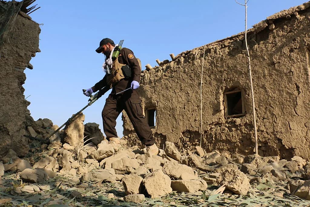 A man in uniform uses a metal detector in a destroyed building.