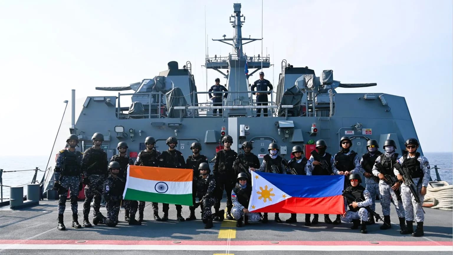 Military personnel from India and the Philippines stand on a ship with their flags.