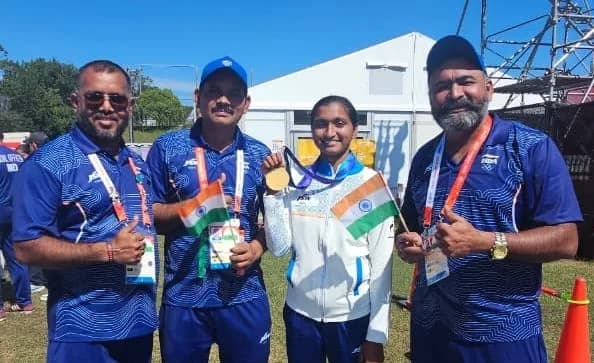 A woman holds a gold medal and Indian flags with coaches.