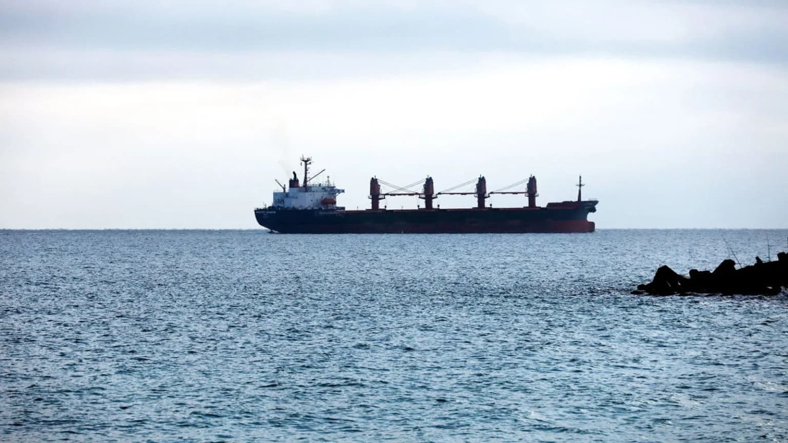 A large cargo ship sails on the sea under a cloudy sky.