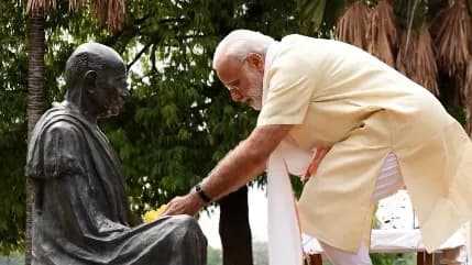 A man in a light-colored tunic places yellow flowers on a statue of a seated man.