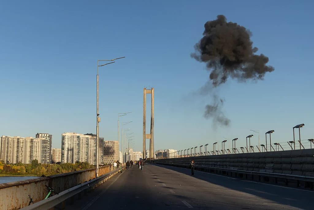 Black smoke billows into the sky over a bridge with buildings in the background.